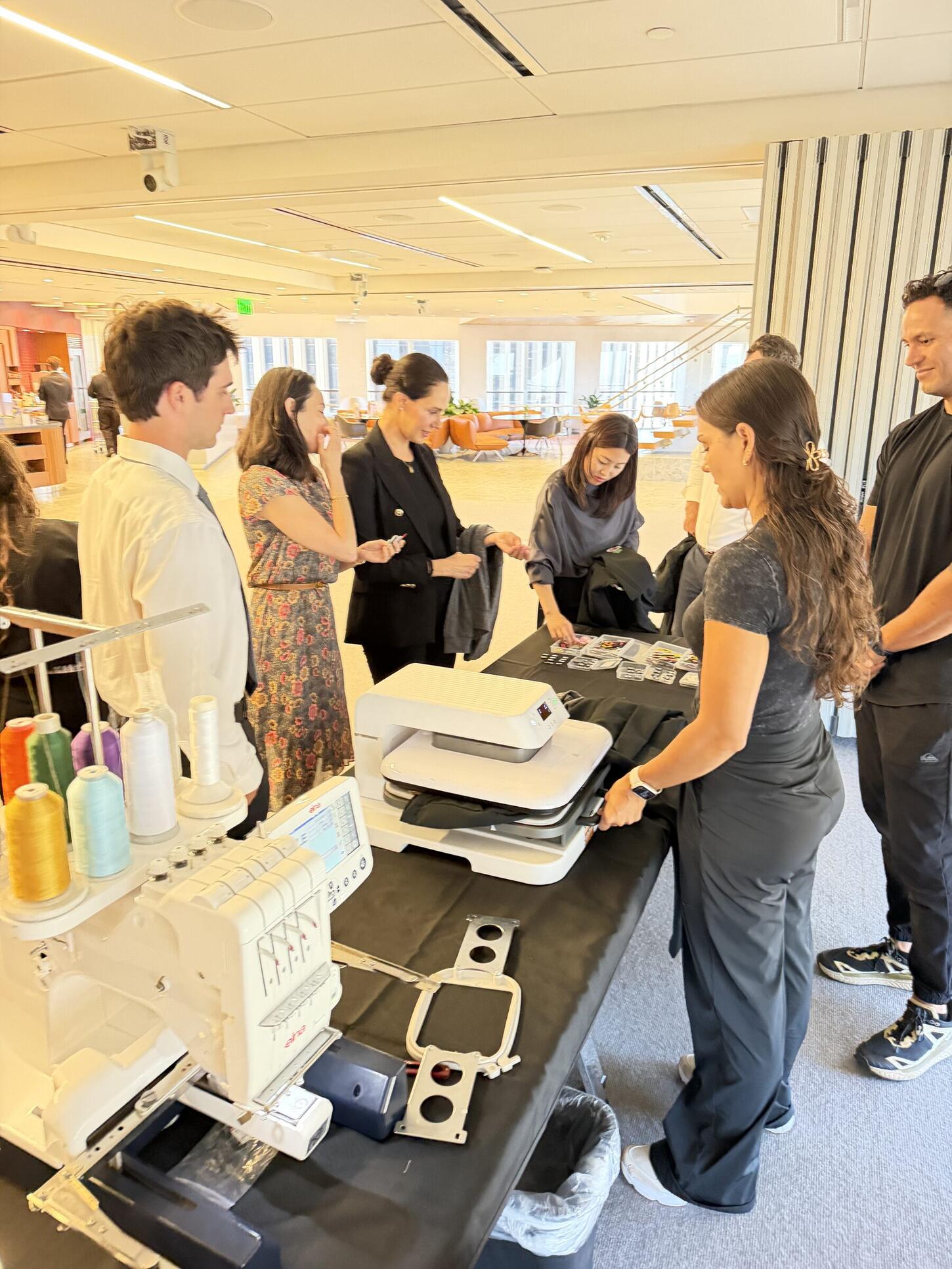 Indoor personalization station with a heat press and an embroidery machine running while guests wait alongside